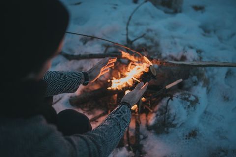 Person warming hands over small campfire on snow-covered ground at dusk