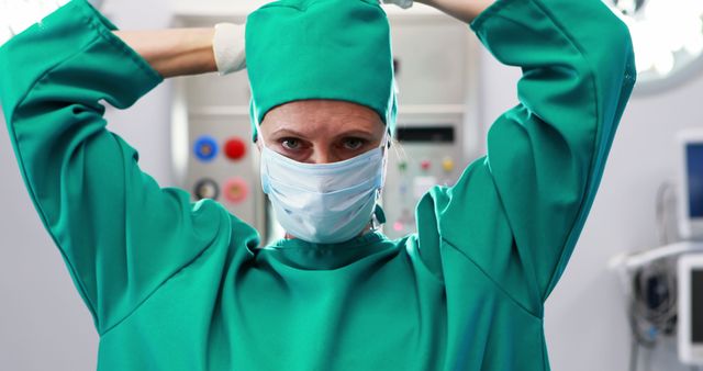 Surgeon dressed in green scrubs and face mask preparing for surgery in a hospital operating room. Perfect for use in medical articles, healthcare promotions, hospital advertising, or educational materials about surgical procedures and healthcare professionals.