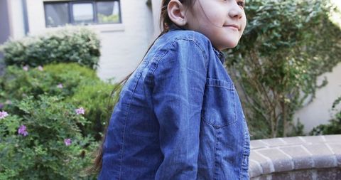 Young girl leaning on curved brick wall in courtyard garden wearing denim jacket, serene