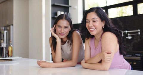 Two friends leaning on modern kitchen island smiling in natural light, casual lifestyle