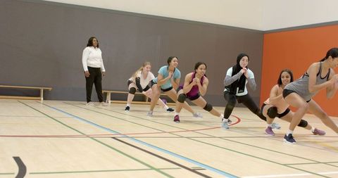 Diverse women performing group squat and lunge workout in indoor gym class
