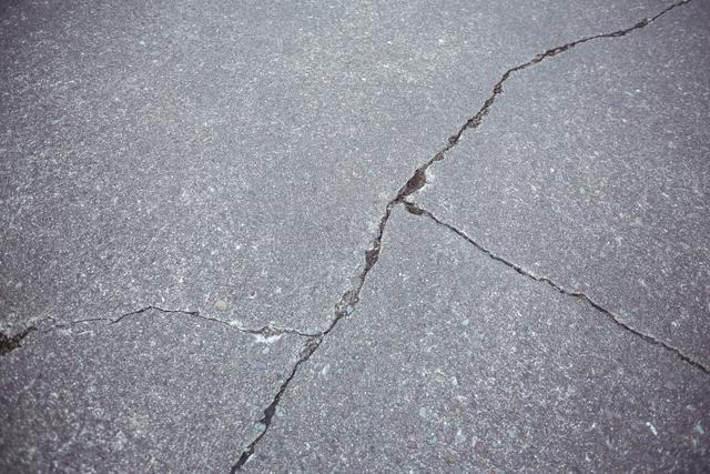 This image shows a close-up view of a cracked asphalt road surface, highlighting the texture and damage. It can be used in articles or presentations about infrastructure maintenance, road construction, urban planning, and the effects of wear and tear on roadways. It is also suitable for illustrating concepts related to transportation, repair, and deterioration of public infrastructure.