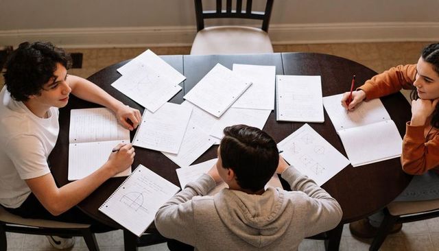 Teens studying together at dining table with notebooks and geometry notes