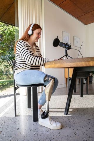 Woman with prosthetic leg working from home with laptop and microphone