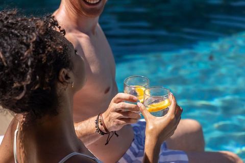 Sunlit poolside toast: couple clinking citrus glasses by blue water