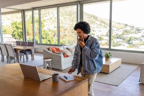 African american man speaking on phone checking laptop in modern open living space