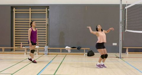 Diverse women teammates practicing volleyball in indoor gymnasium serving and training