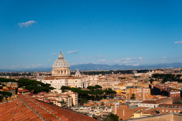 This photo showcases a panoramic view of Vatican City's skyline with the iconic St. Peter's Basilica prominently in the foreground. The clear blue sky adds contrast to the historic architecture. Ideal for use in travel guides, tourism advertisements, educational materials about Rome or the Vatican, and articles discussing historical landmarks in Europe.