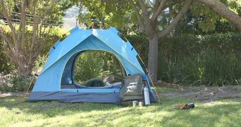 Blue dome tent sitting on grassy backyard lawn with backpack, thermos and sleeping bag