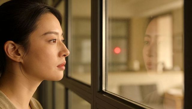 Contemplative woman gazing through office glass with reflective profile and red light
