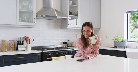 Smiling Woman in Modern Kitchen Checking Smartphone Leisurely