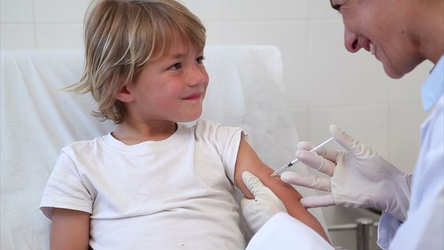 Smiling child receiving an injection from a doctor in a clinical setting. The doctor is wearing gloves and holding a syringe, making the child feel comfortable and at ease. Ideal for use in healthcare advertisements, vaccination awareness campaigns, pediatric care articles, and medical journals.