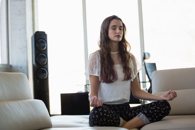 Young businesswoman with eyes closed doing yoga on sofa in office