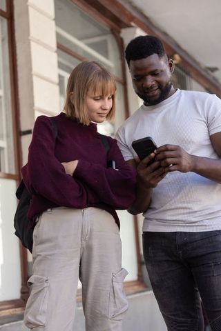 Diverse young adults standing on urban sidewalk checking smartphone and sharing directions