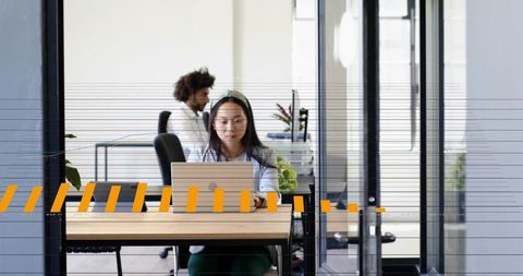 Woman working on laptop in modern open office with glass partitions and orange decals