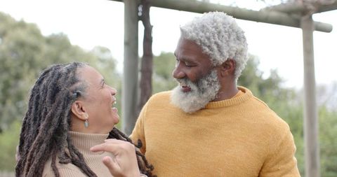 Senior couple laughing and embracing under pergola wearing cozy sweaters and turquoise earrings