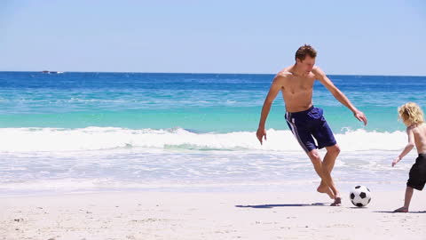 Father and Son Enjoy Beach Soccer Under Sunny Skies