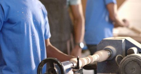 Collaborative woodworking brothers using lathe in dusty workshop