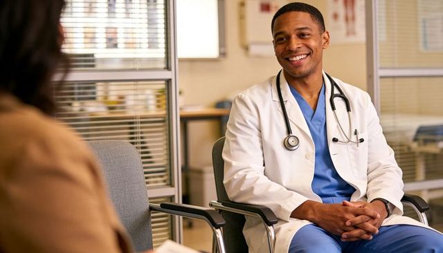 Smiling male doctor consulting patient in modern clinic wearing white coat and blue scrubs