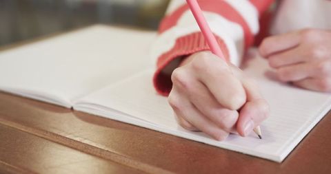 Child Writing in Notebook with Pink Pencil at Wooden Desk