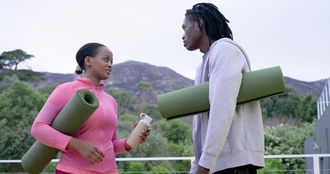 African American couple carrying yoga mats on balcony, chatting for outdoor yoga session