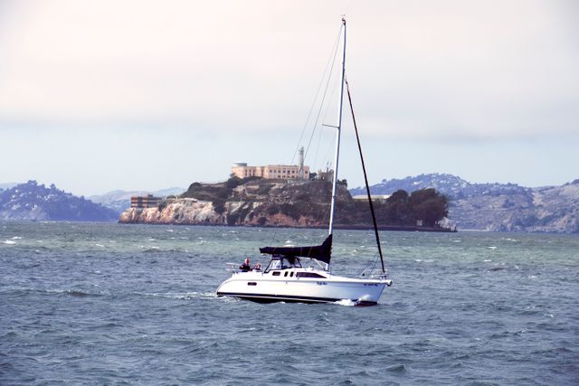 Sailboat glides across open water with distant island visible in background, depicting tranquil marine adventure. Ideal for travel and boating themes, inspiring relaxation, exploration, and oceanic journeys.