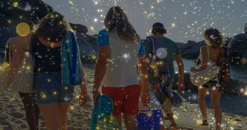 Backlit friends walking toward ocean carrying coolers and beach towels at sunset