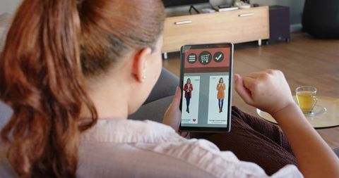 Woman shopping on tablet at home browsing fashion app on couch cozy living room ecommerce