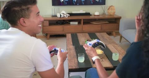 African american couple playing console games on sofa with controllers and snacks