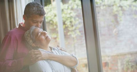 Elderly Couple Embracing by Sunlit Window at Home