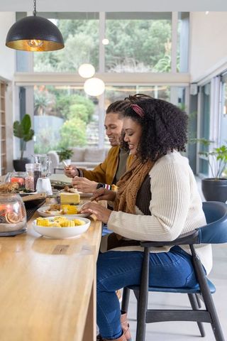 Couple enjoying cozy brunch at sunlit modern kitchen counter with plants and corn on cob