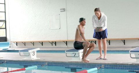 Swimming coach reviews performance with athlete poolside in slow motion