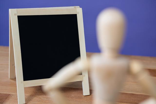 Conceptual image of figurine standing near a chalkboard on a wooden floor