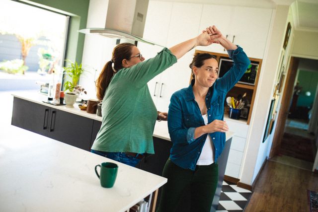 Happy caucasian mature lesbian couple dancing in kitchen at home. unaltered, family, homosexual couple, lgbtqia people, lifestyle, leisure activity and domestic life.
