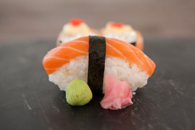 Close-up of nigiri and uramaki sushi served on black stone slate on wooden table