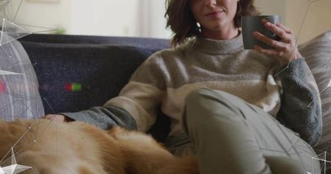 Woman relaxing on sofa sipping coffee while petting golden retriever cozy home moment