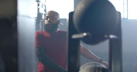 African american man preparing for lift in industrial gym wearing maroon shirt and smartwatch