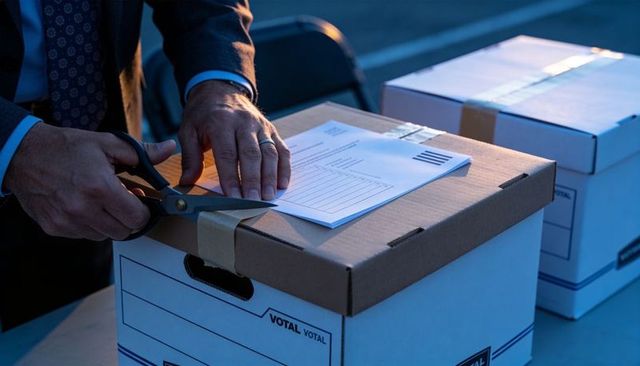 Poll worker cutting tape on ballot box while securing ballots and documents at dusk