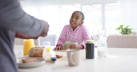 African american father reaching in kitchen while daughter holding cereal bowl morning