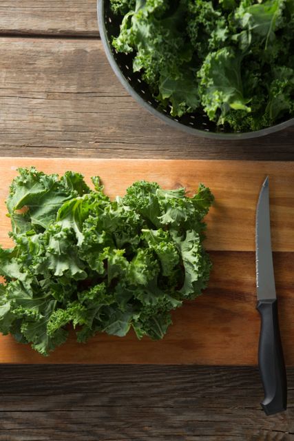 Overhead view of fresh kale with knife on cutting board at wooden table
