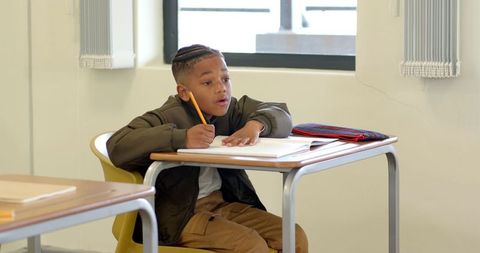 African american boy writing in classroom seated at desk