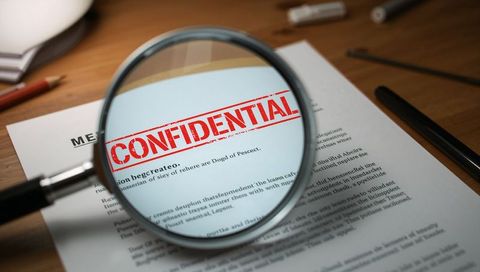 Magnifying glass revealing confidential stamp on document with pen and pencil