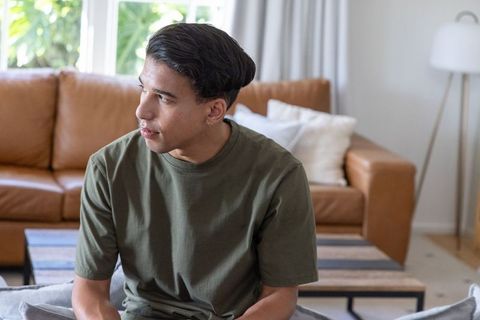 African american man sitting on leather sofa looking away in bright modern living room