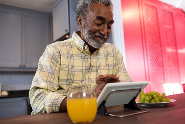 Happy senior man using tablet computer at table in kitchen