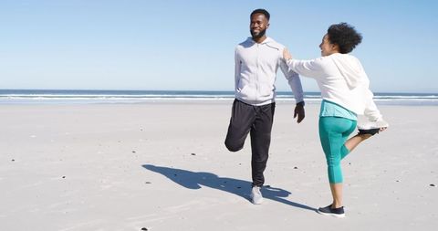 Couple stretching on beach before run, smiling and warming up along sunny ocean shoreline
