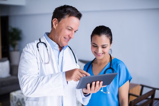 Doctors are collaborating and discussing patient care using a digital tablet in a hospital setting. Both are smiling and appear engaged, indicating a positive and professional environment. This image can be used for healthcare-related content, medical technology promotions, teamwork in healthcare, and modern medical practices.