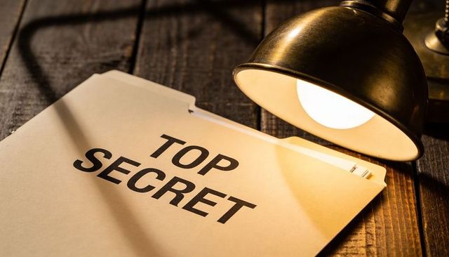 Top secret file under desk lamp revealing confidential documents on wooden table with warm lamp glow