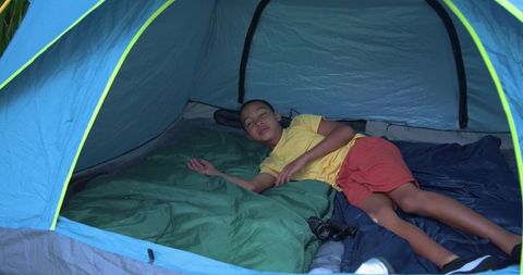 Young african american boy resting in blue tent on camping trip with binoculars