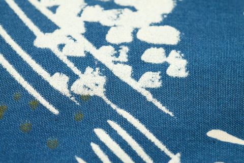 Close-up showing blue indigo fabric featuring white hand-printed floral lines and texture