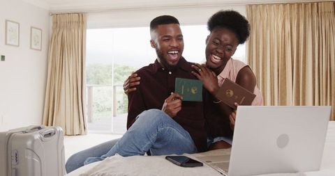 Joyful Couple Celebrating Travel Plans at Home with Laptops and Passports